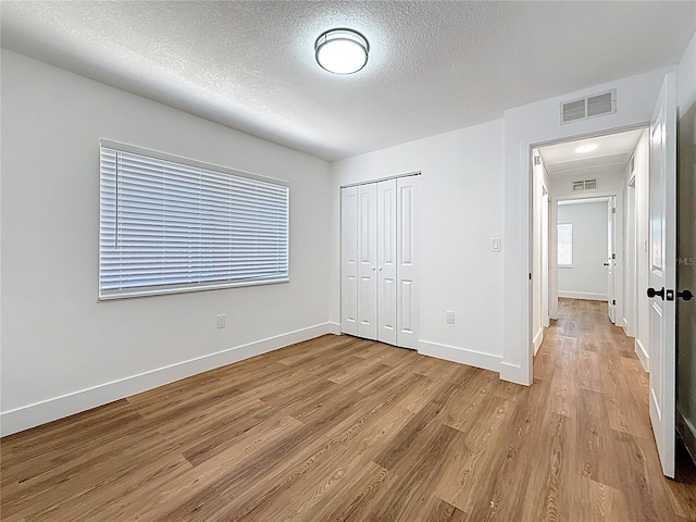 unfurnished bedroom featuring light wood-style floors, visible vents, a closet, and baseboards