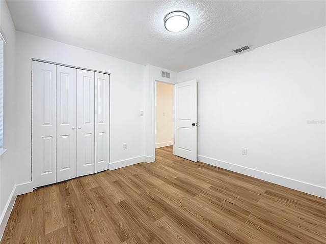 unfurnished bedroom featuring visible vents, baseboards, a textured ceiling, and wood finished floors