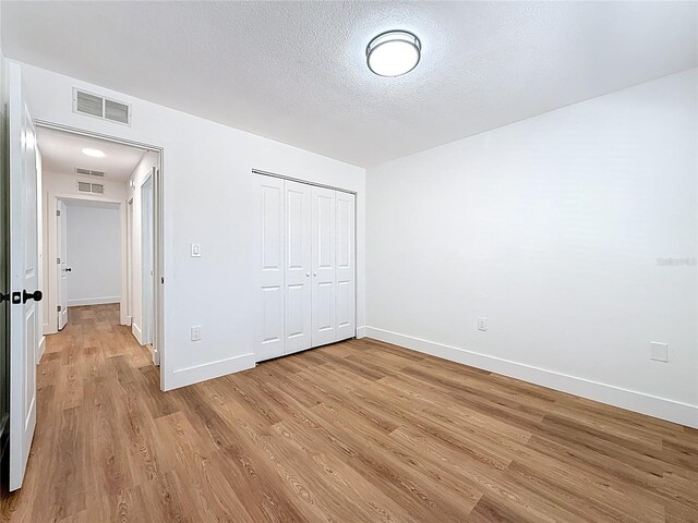 unfurnished bedroom with light wood-type flooring, visible vents, a textured ceiling, a closet, and baseboards