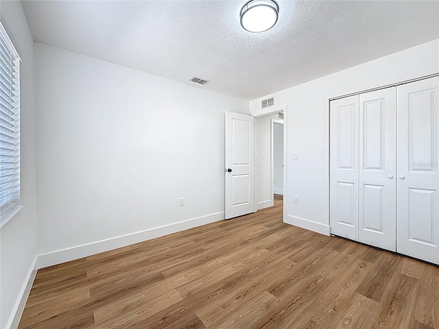 unfurnished bedroom featuring a closet, visible vents, a textured ceiling, and light wood-style floors