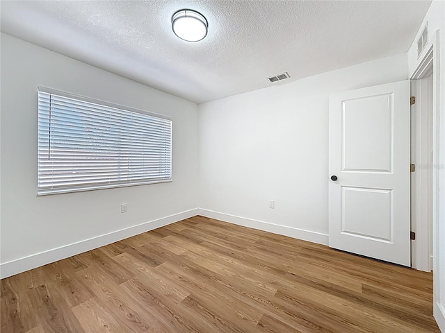 empty room with visible vents, a textured ceiling, baseboards, and wood finished floors