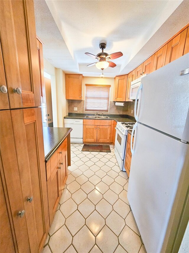 kitchen with a sink, decorative backsplash, white appliances, and dark countertops