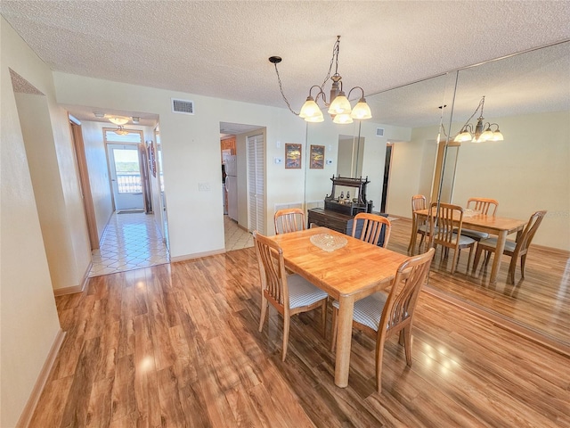 dining area with a chandelier, visible vents, a textured ceiling, and light wood-style floors