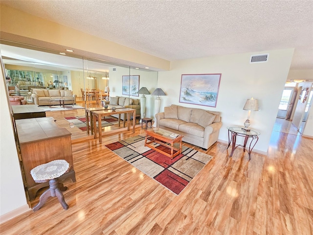 living area with baseboards, wood finished floors, visible vents, and a textured ceiling