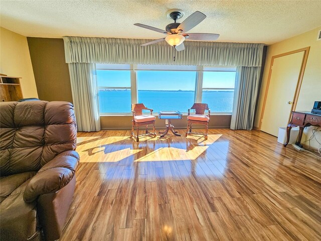 living room with a ceiling fan, wood finished floors, a water view, and a textured ceiling