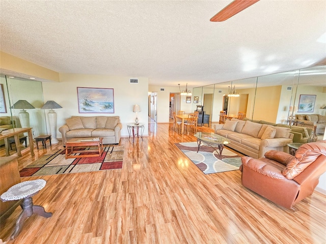 living area with visible vents, a textured ceiling, light wood-style flooring, and ceiling fan with notable chandelier