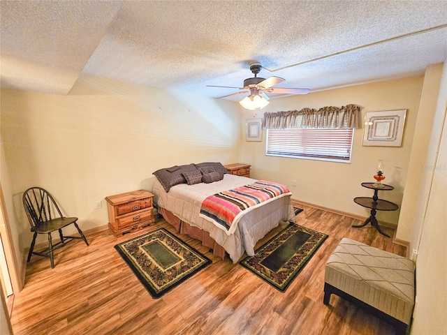 bedroom featuring ceiling fan, a textured ceiling, baseboards, and wood finished floors