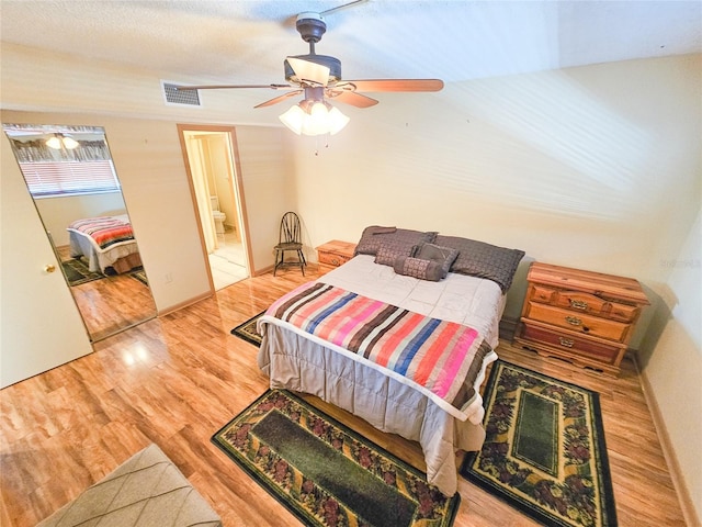 bedroom featuring visible vents, ensuite bath, a ceiling fan, and wood finished floors