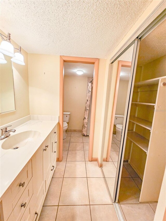 full bathroom featuring toilet, a textured ceiling, tile patterned flooring, baseboards, and vanity