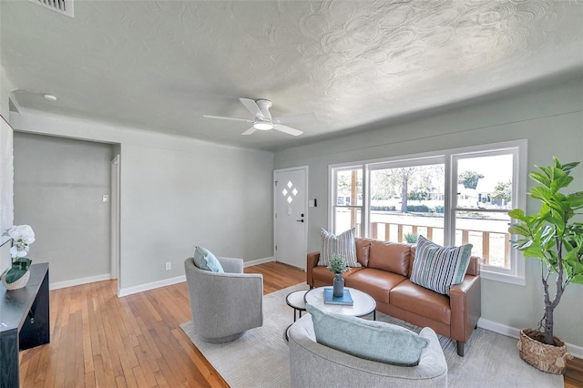 living area with a ceiling fan, baseboards, light wood-type flooring, and a textured ceiling