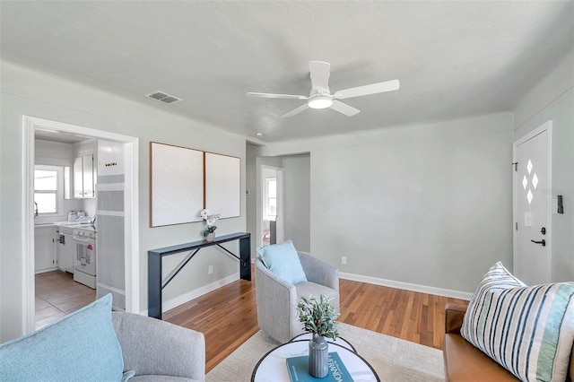 living area featuring visible vents, baseboards, a ceiling fan, and light wood finished floors