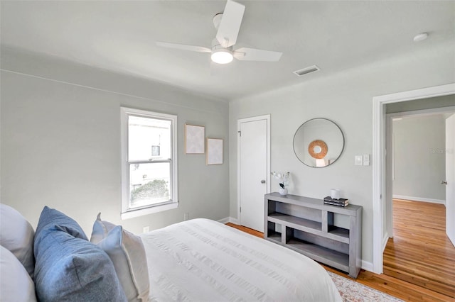 bedroom with a ceiling fan, wood finished floors, visible vents, and baseboards