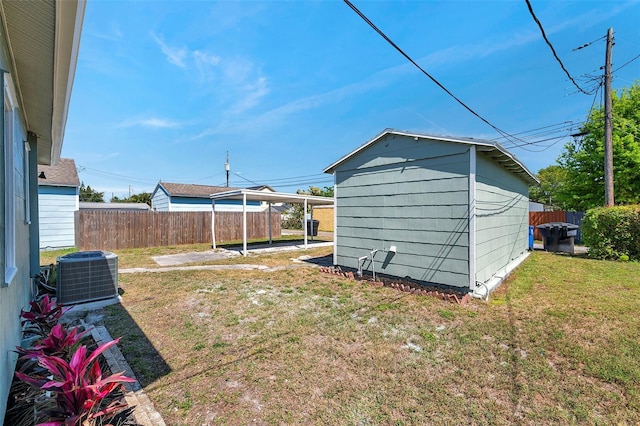 view of yard featuring a carport, fence, central air condition unit, a shed, and an outbuilding