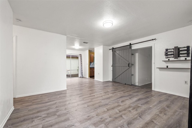 empty room with a barn door, wood finished floors, baseboards, and a textured ceiling