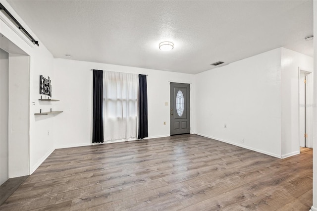 entryway featuring visible vents, a textured ceiling, wood finished floors, a barn door, and baseboards