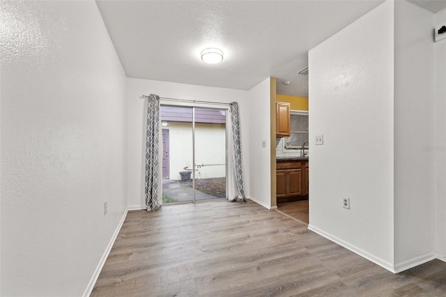 unfurnished dining area featuring light wood finished floors, a textured ceiling, and baseboards