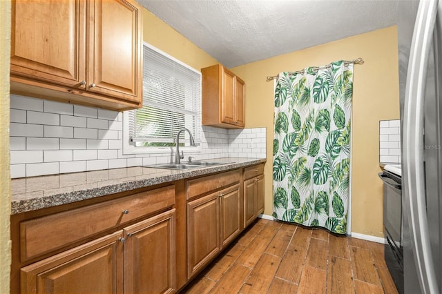 kitchen with light wood finished floors, freestanding refrigerator, a sink, decorative backsplash, and electric stove