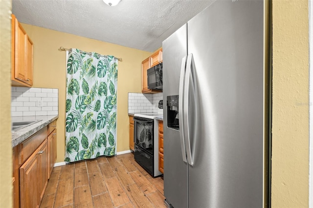 kitchen with black microwave, light wood-type flooring, stainless steel refrigerator with ice dispenser, electric range, and a sink