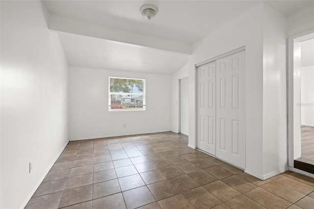 unfurnished bedroom with a closet, baseboards, vaulted ceiling, and tile patterned flooring