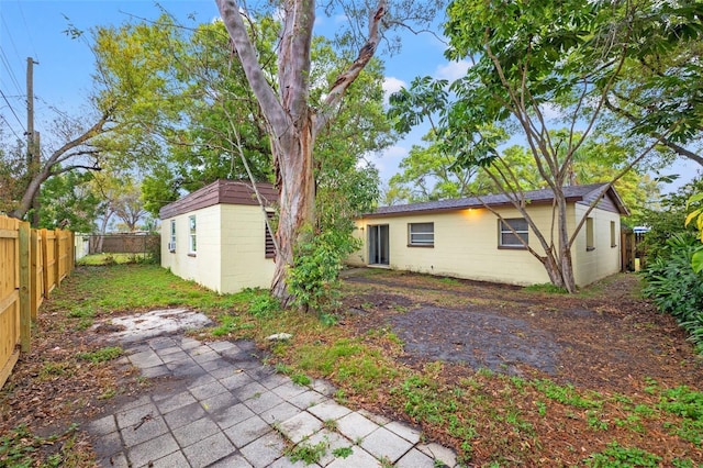 rear view of house featuring a patio, concrete block siding, a fenced backyard, and an outdoor structure