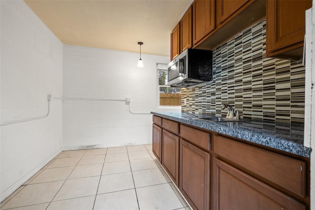 kitchen featuring a sink, stainless steel microwave, dark countertops, brown cabinetry, and decorative backsplash