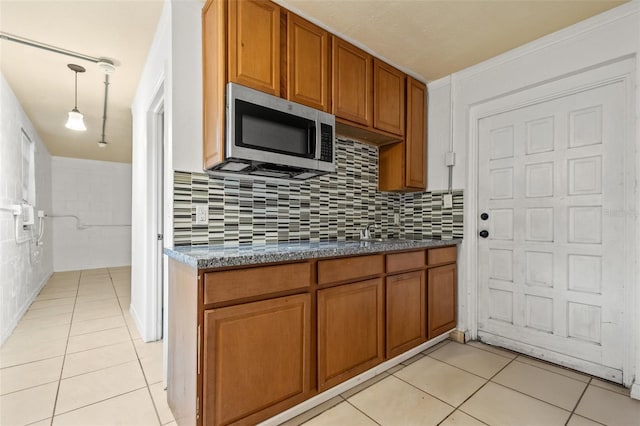 kitchen with brown cabinets, stainless steel microwave, backsplash, light tile patterned floors, and hanging light fixtures