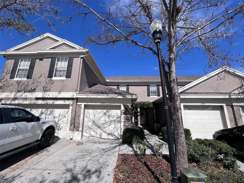 view of front of home with stucco siding, roof with shingles, and concrete driveway