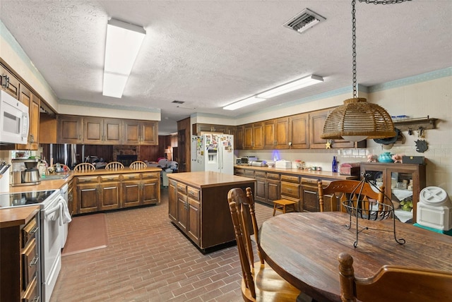 kitchen with white appliances, visible vents, a kitchen island, brick floor, and wood counters