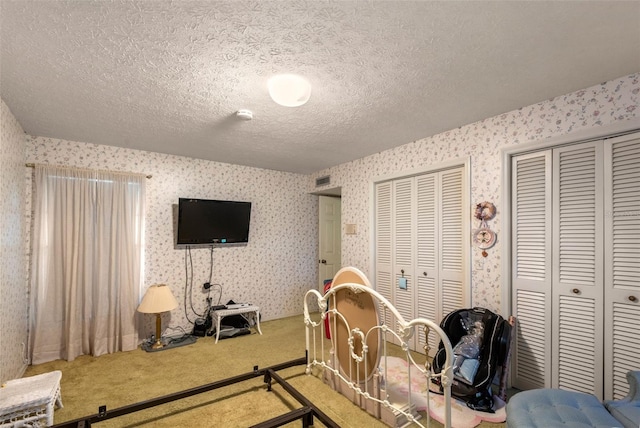 carpeted bedroom with a textured ceiling, two closets, and wallpapered walls