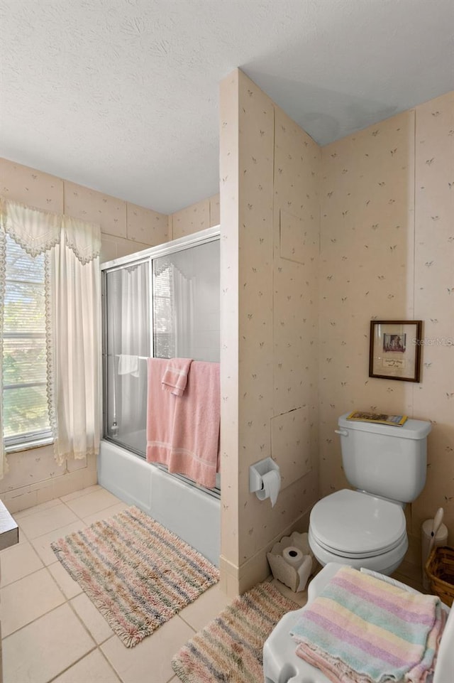 full bath with tile patterned flooring, a textured ceiling, toilet, and bath / shower combo with glass door