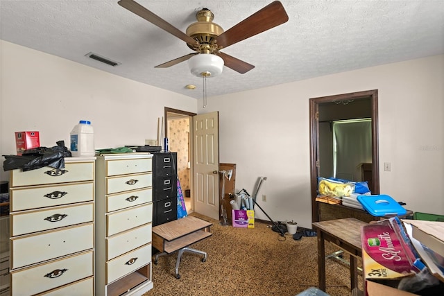 carpeted home office featuring a ceiling fan, visible vents, and a textured ceiling