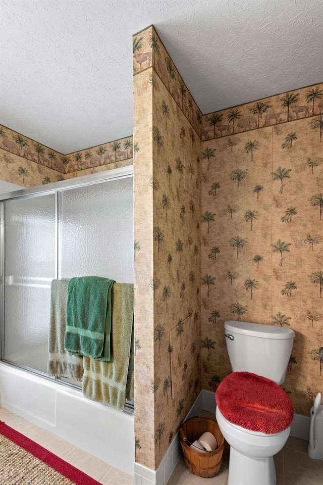 full bath featuring toilet, a textured ceiling, shower / bath combination with glass door, wallpapered walls, and tile patterned flooring