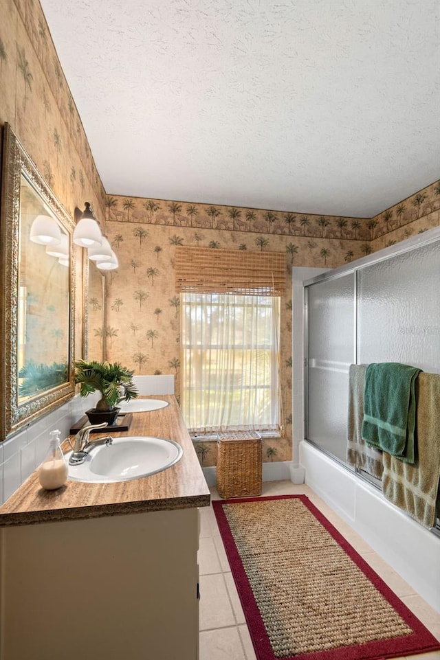 full bath featuring wallpapered walls, double vanity, a sink, a textured ceiling, and tile patterned floors