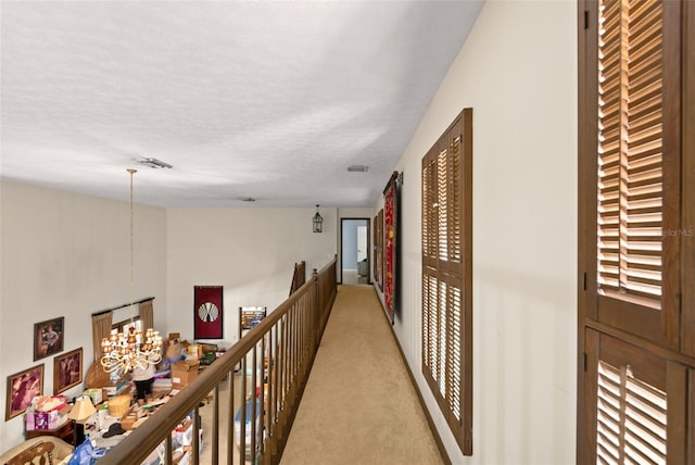 corridor with a textured ceiling, an upstairs landing, visible vents, and light carpet