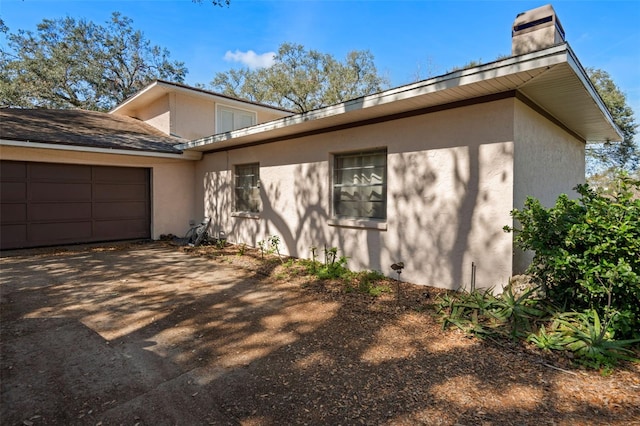 view of side of home featuring stucco siding, driveway, a chimney, and a garage