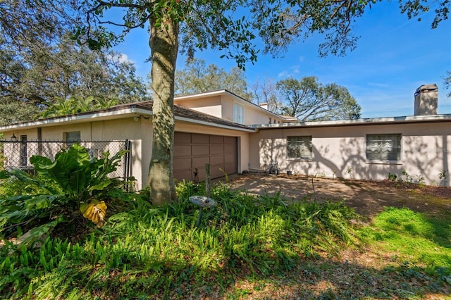 view of front of home with stucco siding, a chimney, a garage, and fence