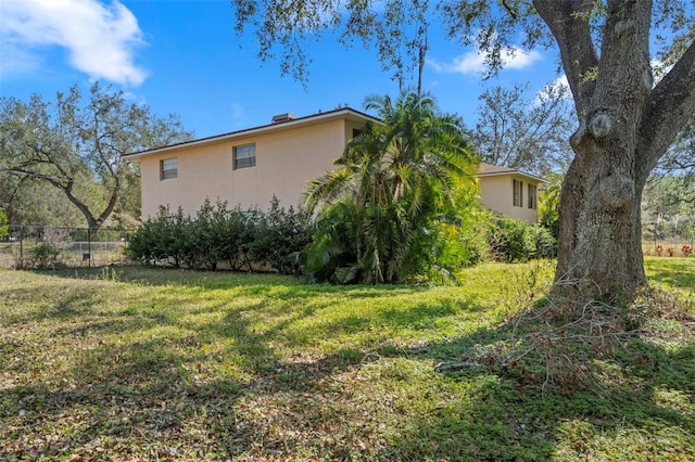 view of side of property with stucco siding, a lawn, and fence