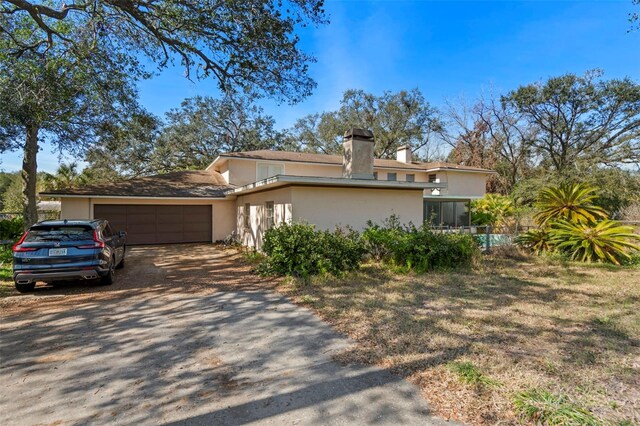 view of front of home with stucco siding, a garage, a chimney, and dirt driveway