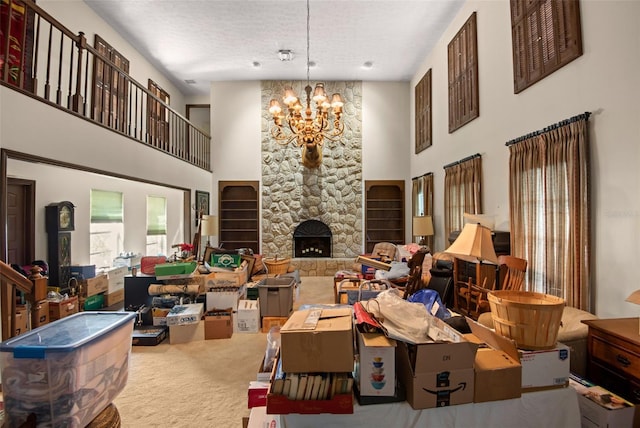 carpeted living area with a textured ceiling, a high ceiling, a stone fireplace, and an inviting chandelier