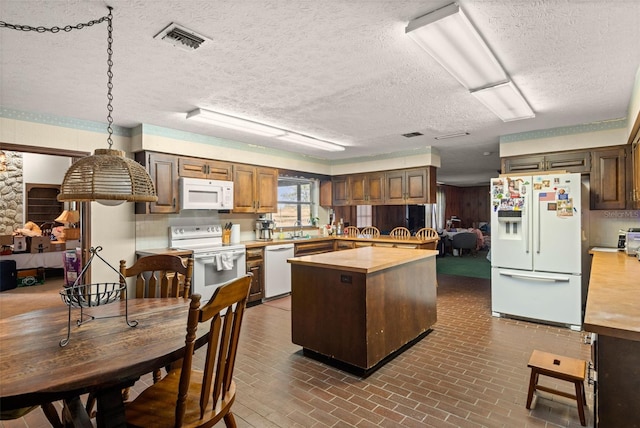 kitchen featuring white appliances, visible vents, a sink, brick patterned floor, and a center island