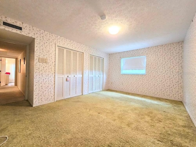 11327 Carter Grove Ln, Thonotosassa, FL 33592 - unfurnished bedroom with wallpapered walls, a textured ceiling, carpet flooring, and multiple closets