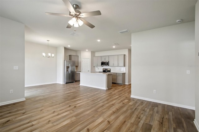 unfurnished living room with a sink, baseboards, light wood-style flooring, and ceiling fan with notable chandelier