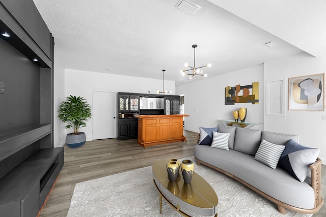 living area with an inviting chandelier, wood finished floors, visible vents, and a textured ceiling