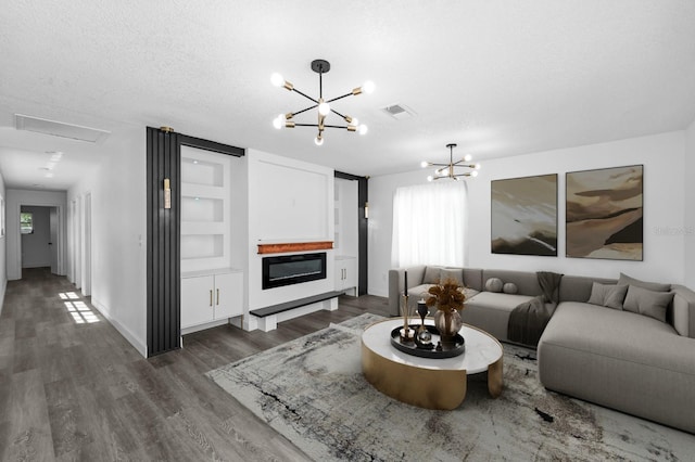 living area with visible vents, a textured ceiling, a glass covered fireplace, an inviting chandelier, and dark wood-style flooring