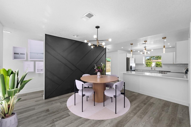 dining room with visible vents, baseboards, wood finished floors, a notable chandelier, and a textured ceiling