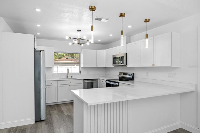 kitchen featuring visible vents, a sink, wood finished floors, appliances with stainless steel finishes, and a peninsula