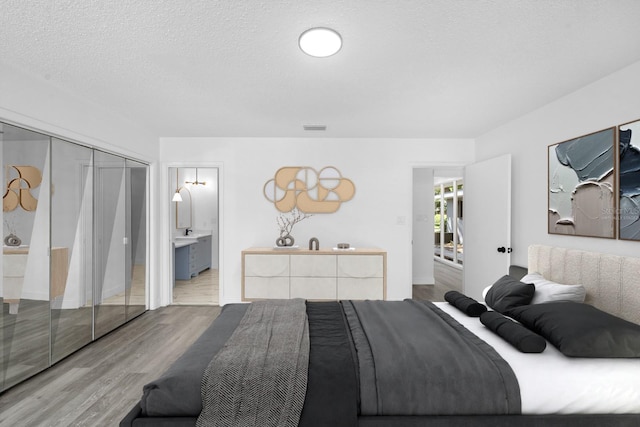 bedroom featuring visible vents, a textured ceiling, wood finished floors, and ensuite bathroom