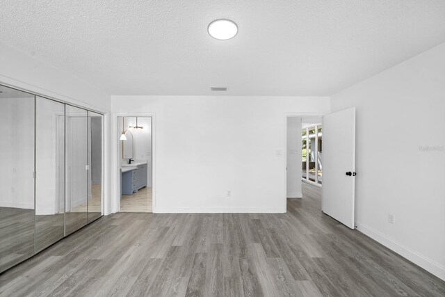 unfurnished bedroom featuring wood finished floors, baseboards, visible vents, ensuite bathroom, and a textured ceiling