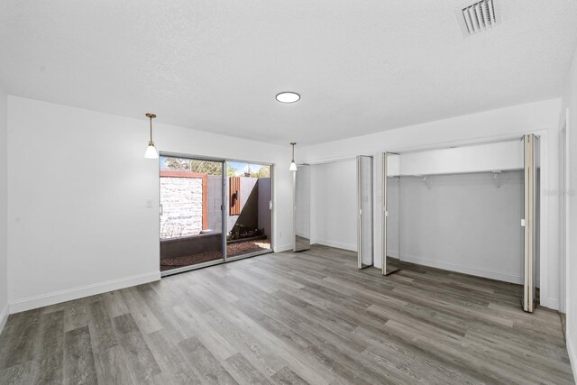 unfurnished bedroom with visible vents, multiple closets, baseboards, and wood finished floors