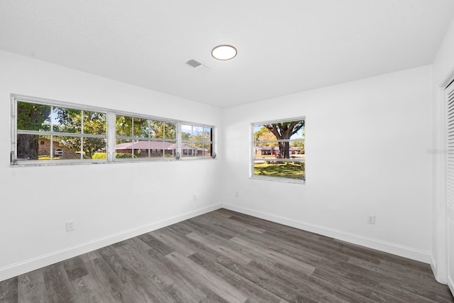 empty room with dark wood-style floors, visible vents, and baseboards